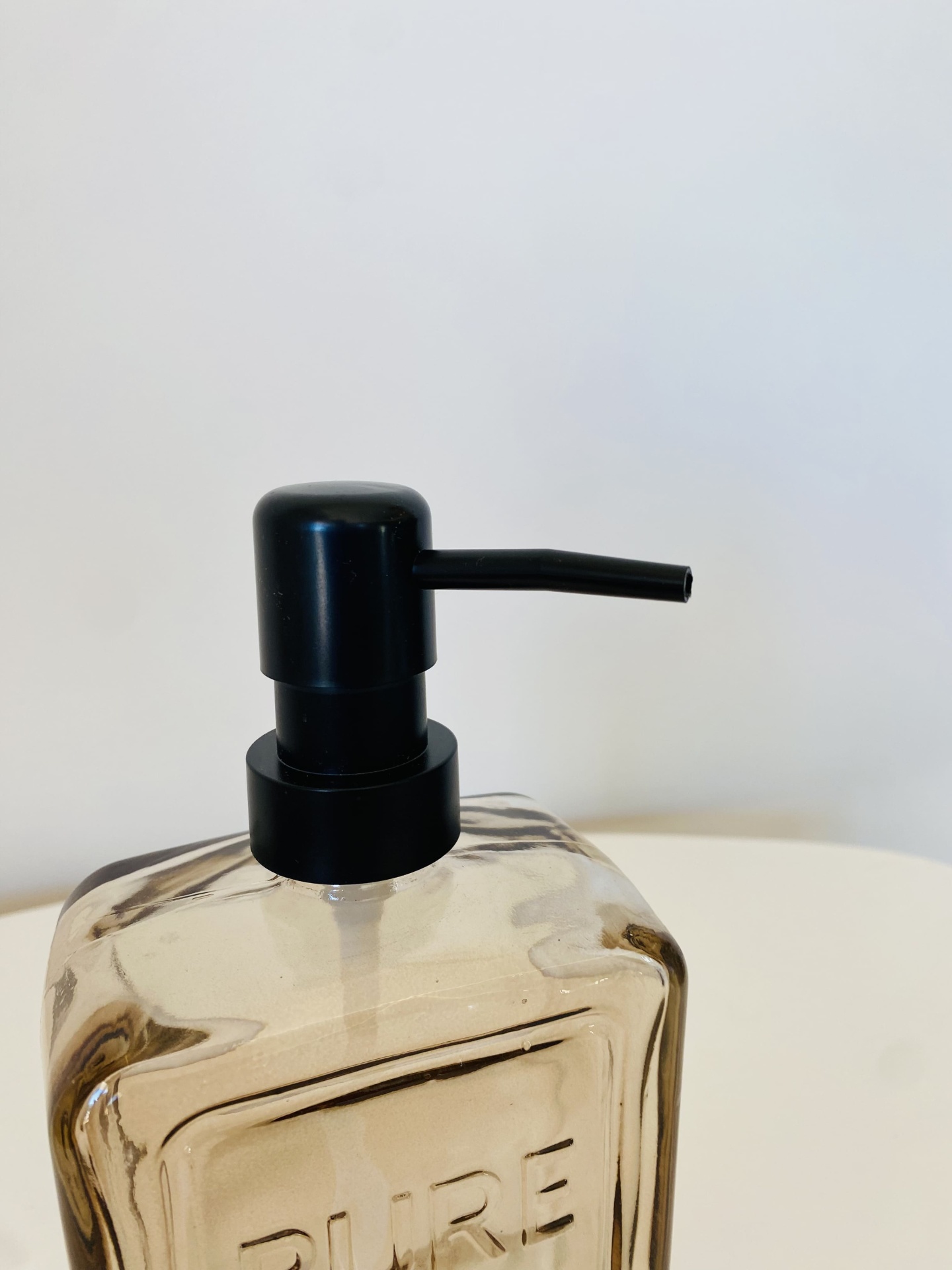 Recipiente doseador transparente castanho com tampa preta e palavra PURE
