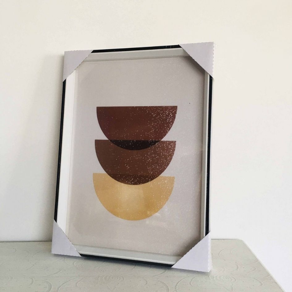 Quadro decorativo com formas semicirculares castanhas e amarelas numa moldura preta