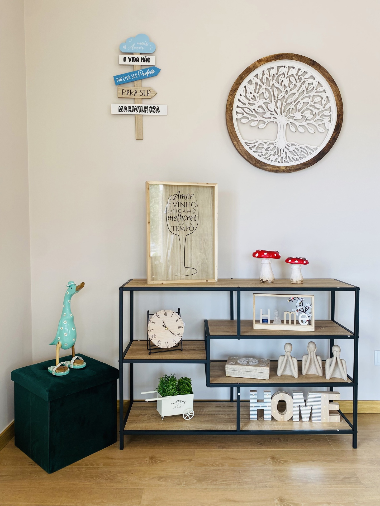 Estante decorativa com itens em madeira e metal, parede branca decorada com árvore e placas de texto.