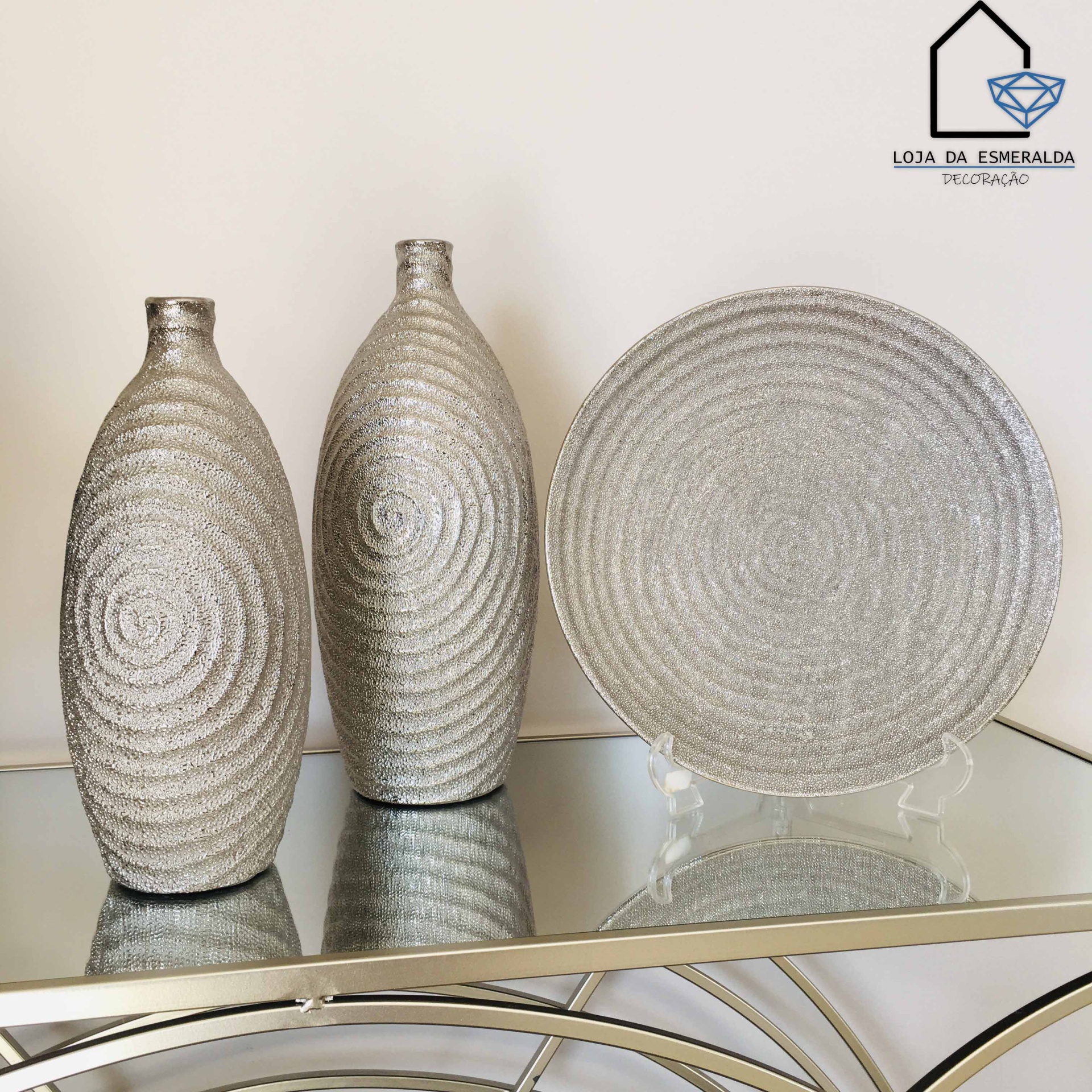 Dois jarros e um prato redondo prateados com textura espiral em superfície espelhada