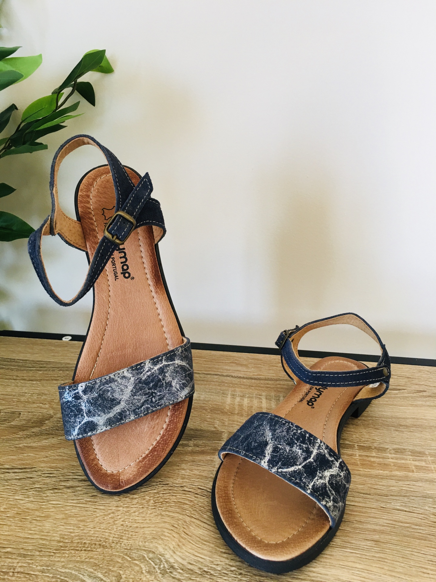 Par de sandálias femininas com padrão marmorizado e tiras pretas sobre superfície de madeira.