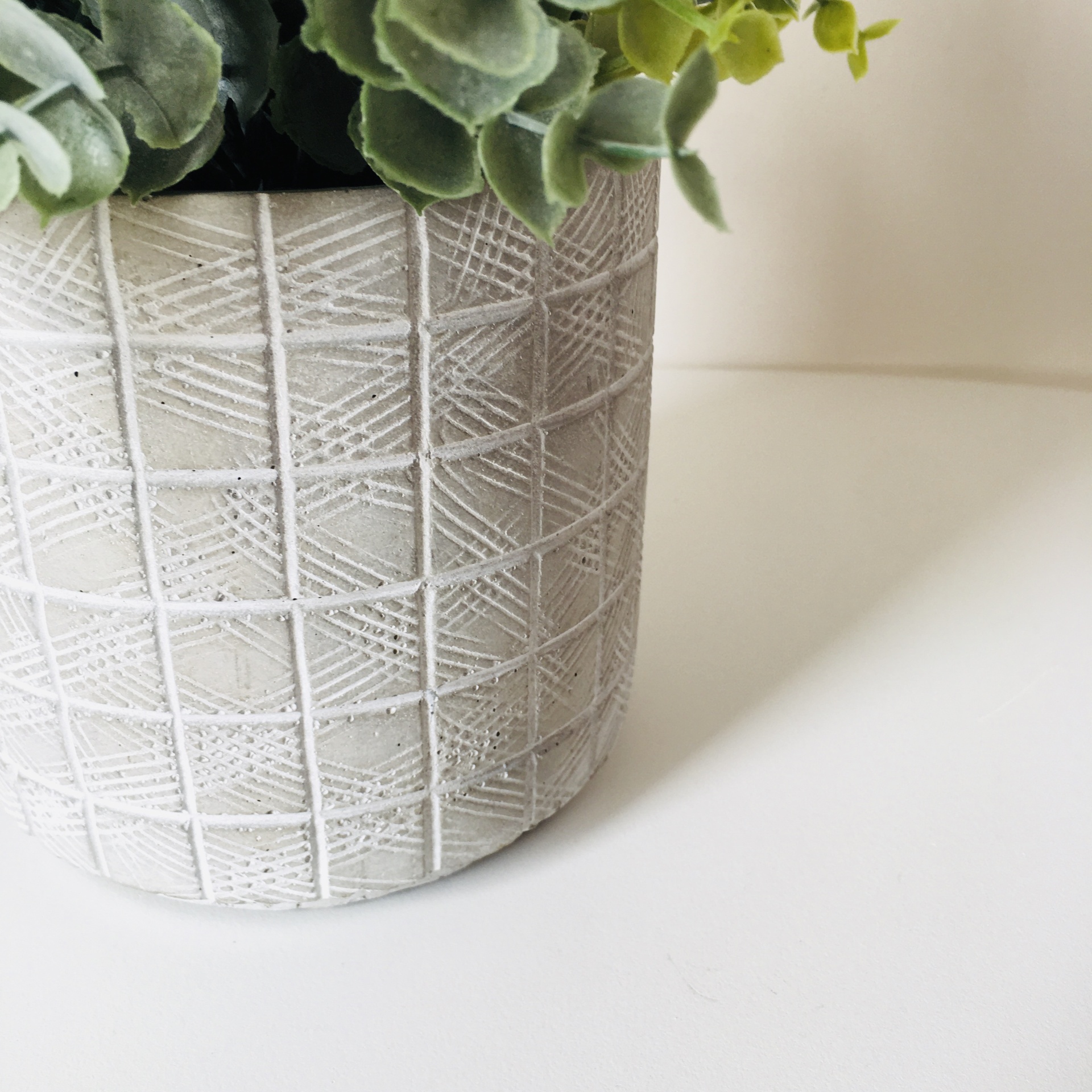 Vaso cinzento claro com padrão geométrico e folhagem verde artificial
