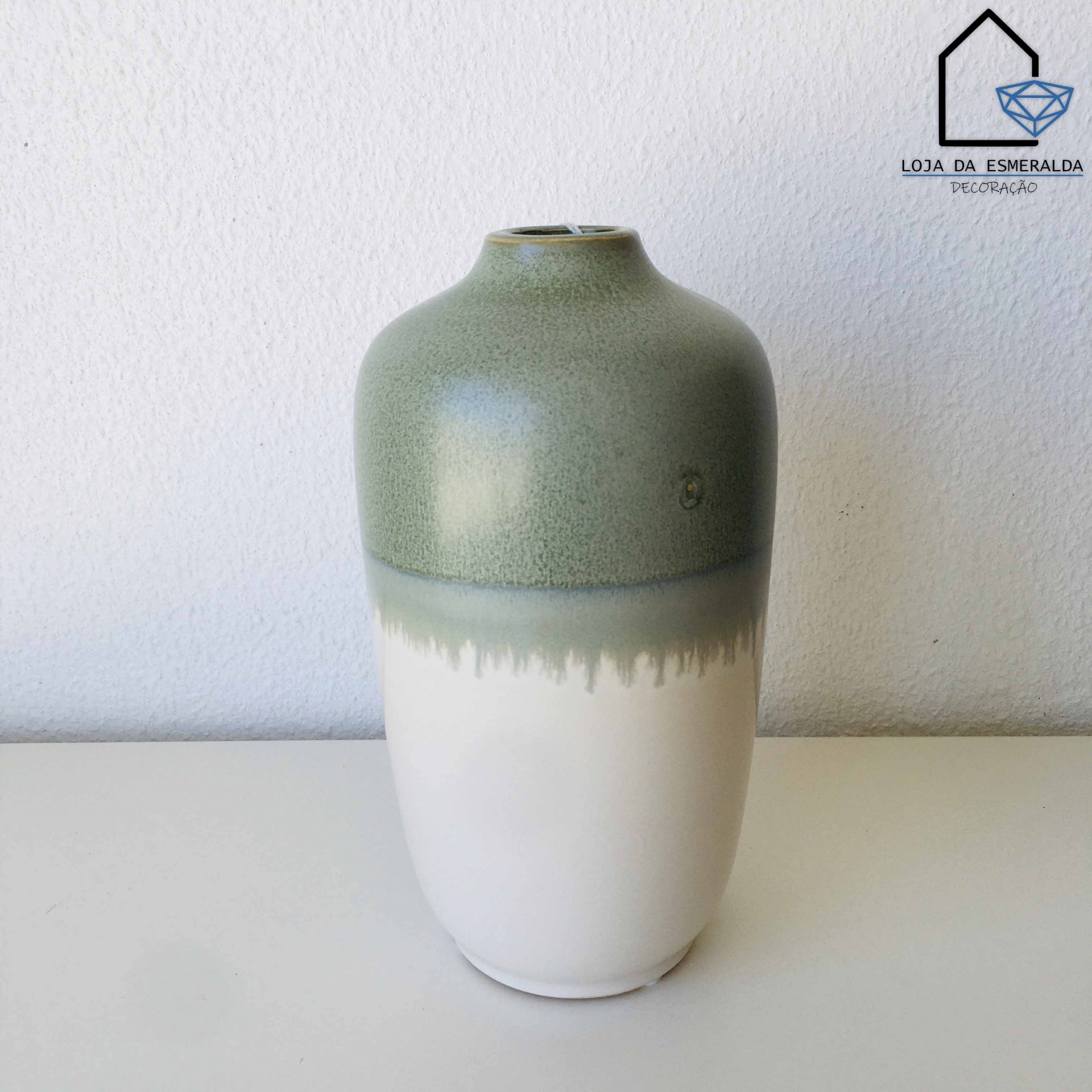 Vaso cerâmico bicolor verde e branco sobre mesa branca com parede ao fundo e logo Loja da Esmeralda
