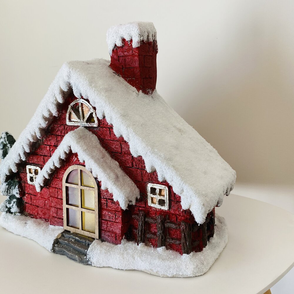 Casa decorativa vermelha com neve artificial no telhado e detalhes de janelas e porta