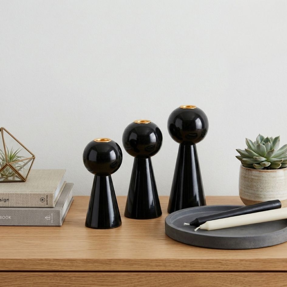 Conjunto de três castiçais pretos brilhantes, velas e planta suculenta sobre mesa de madeira.