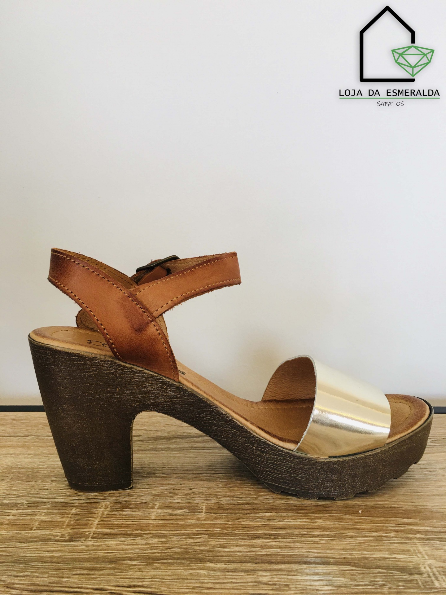 Sandália de salto alto castanha e dourada sobre superfície de madeira