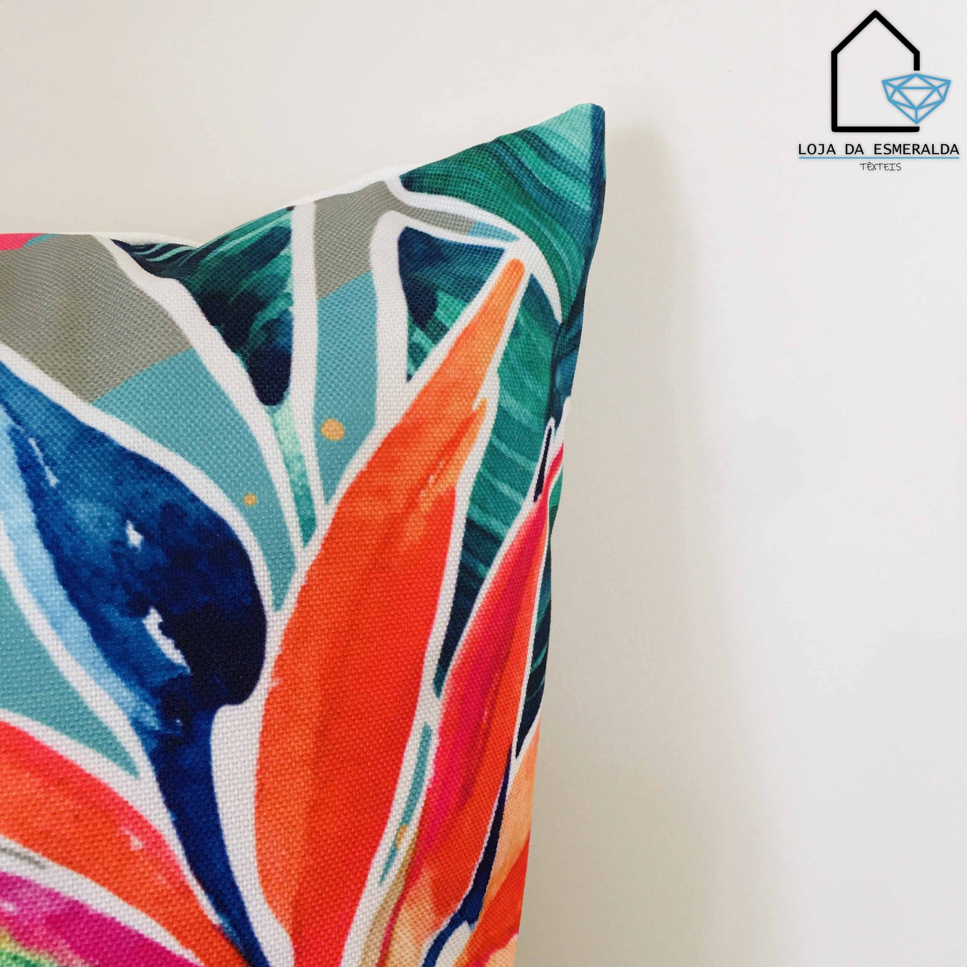 Almofada com padrão floral multicolorido e logo Loja da Esmeralda no canto superior direito