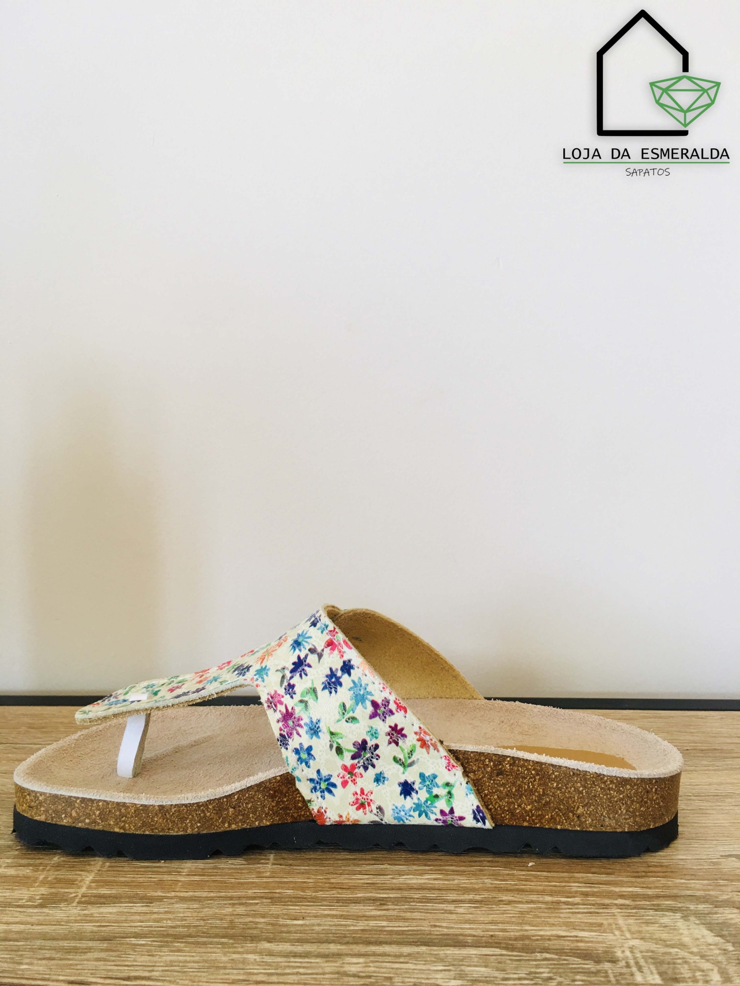 Sandália de cortiça com tiras florais coloridas sobre superfície de madeira clara