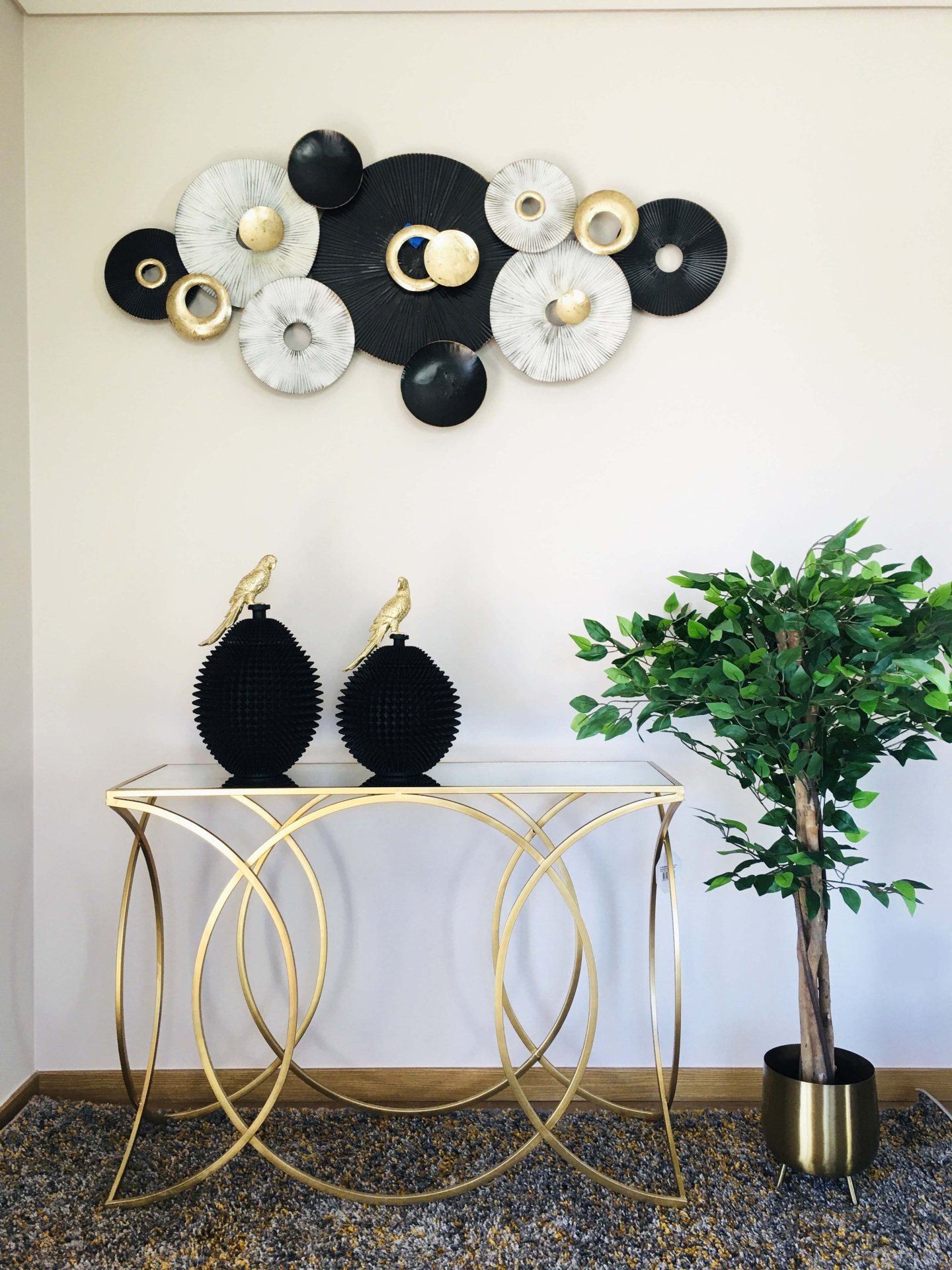 Mesa dourada com esculturas pretas e planta decorativa junto a arte de parede circular colorida.