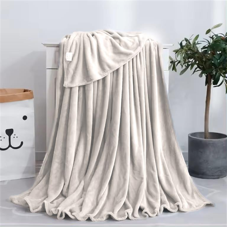 Manta bege suave pendurada em móvel branco, planta e saco com rosto de urso ao lado.