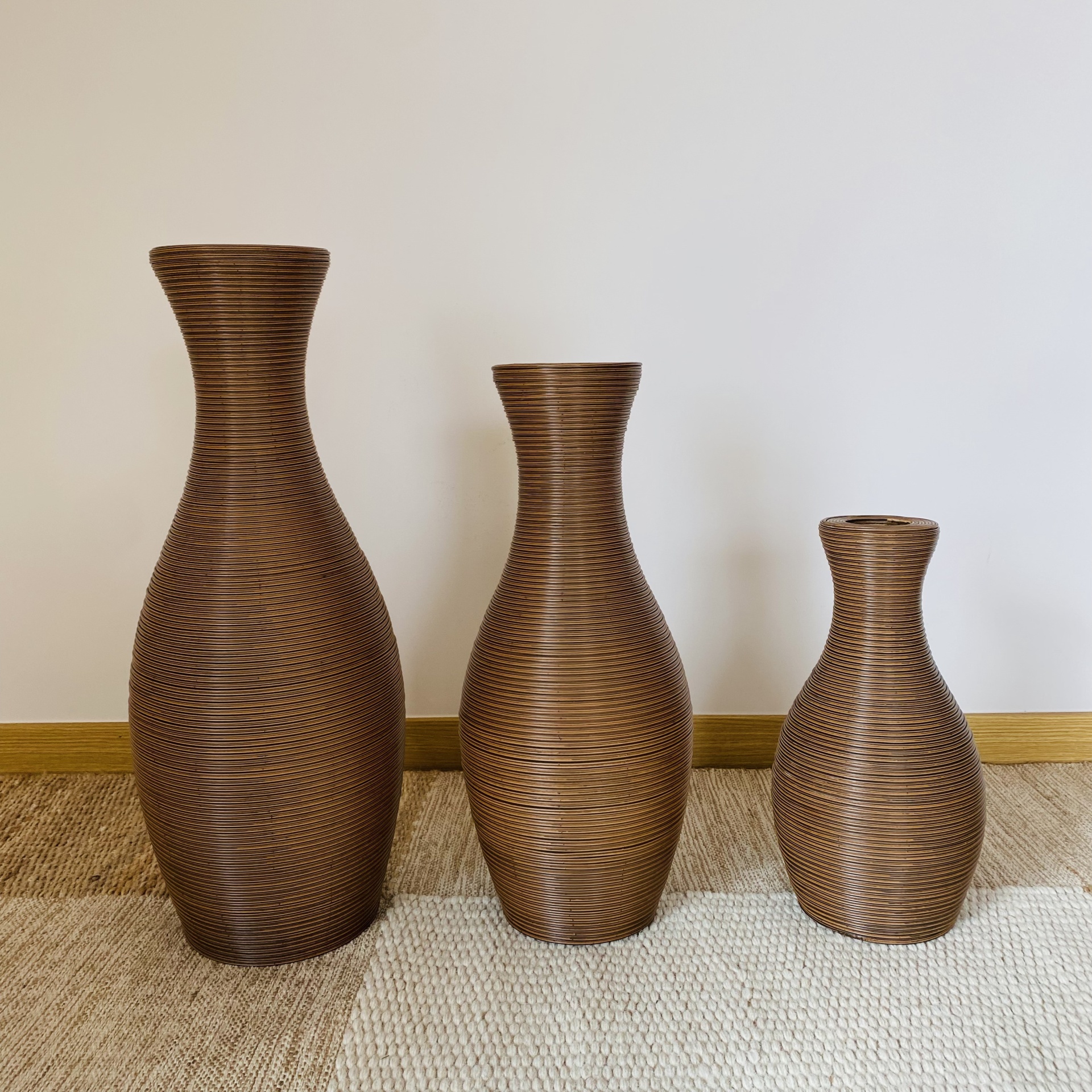 Três vasos castanhos com textura de linhas, em diferentes tamanhos, sobre tapetes bege e castanho. 