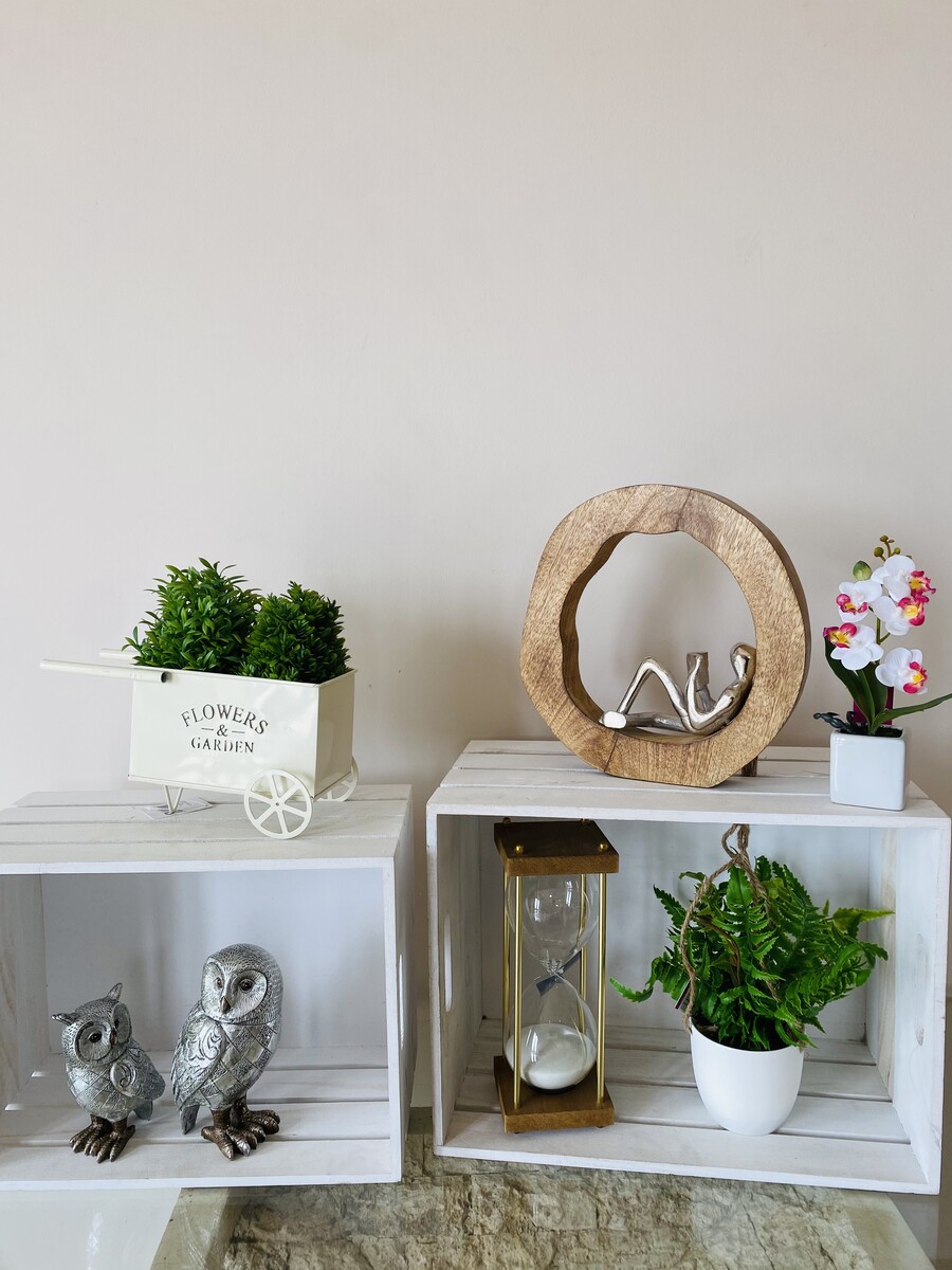 Decoração com plantas artificiais, corujas metálicas, ampulheta, e objeto decorativo em caixotes de madeira branca