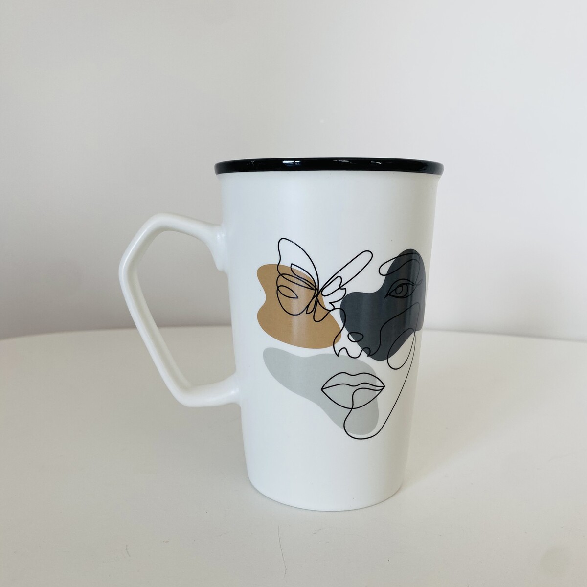 Caneca branca com desenho abstrato de rosto e borboleta colorida.