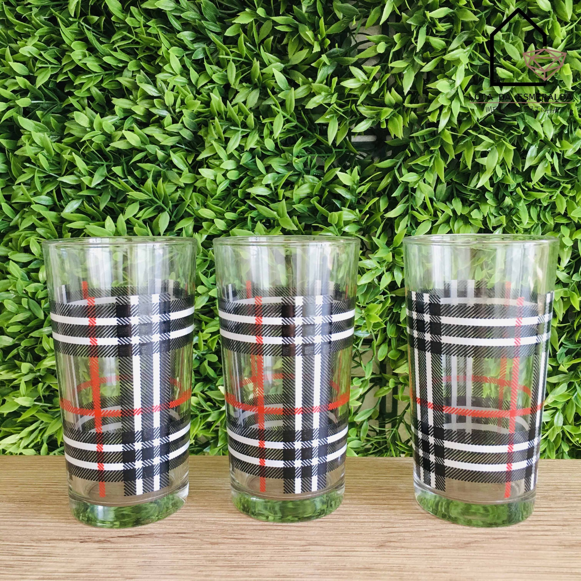 Três copos de vidro com padrão xadrez em fundo de plantas verdes