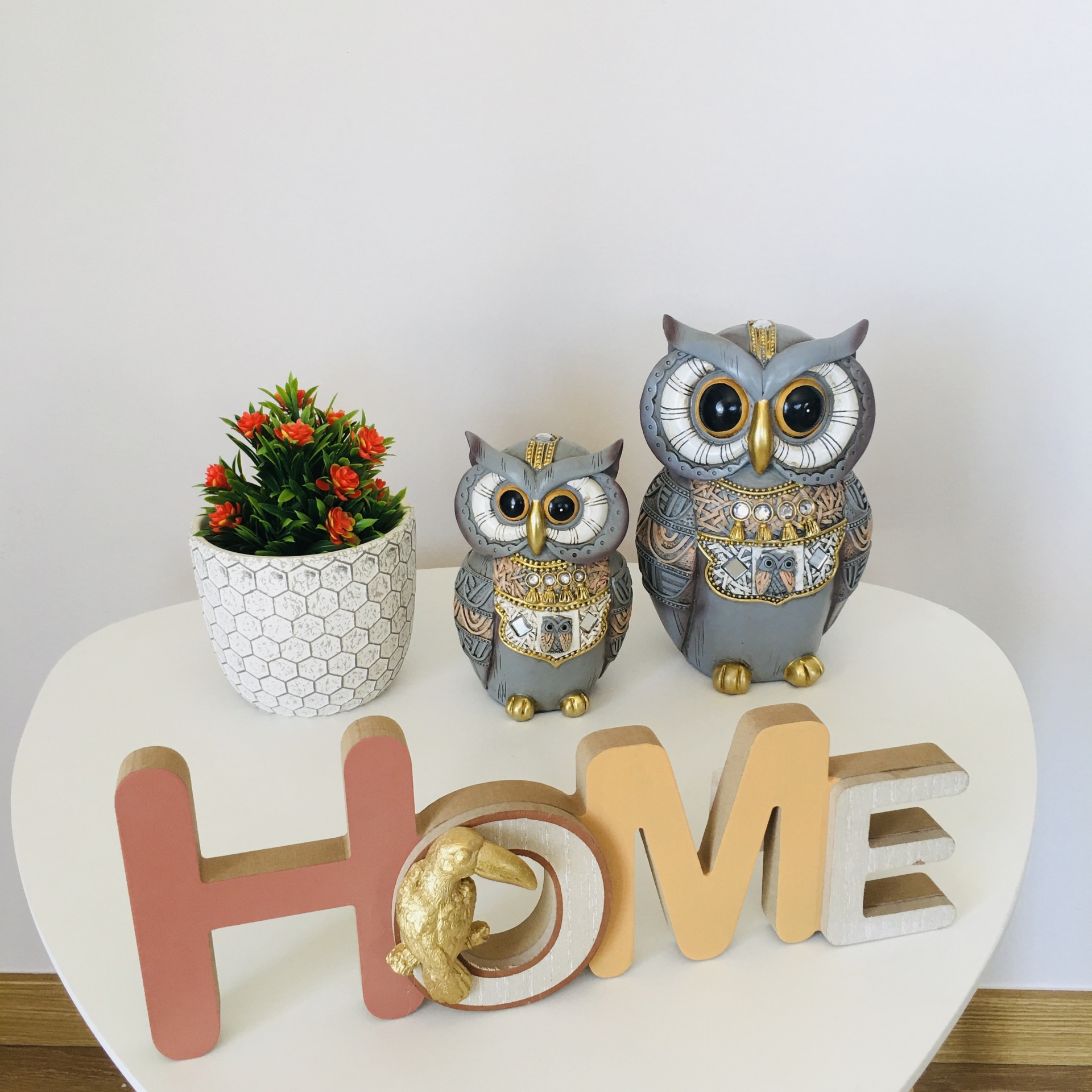 Conjunto decorativo com corujas, vaso de planta e palavra HOME sobre mesa branca