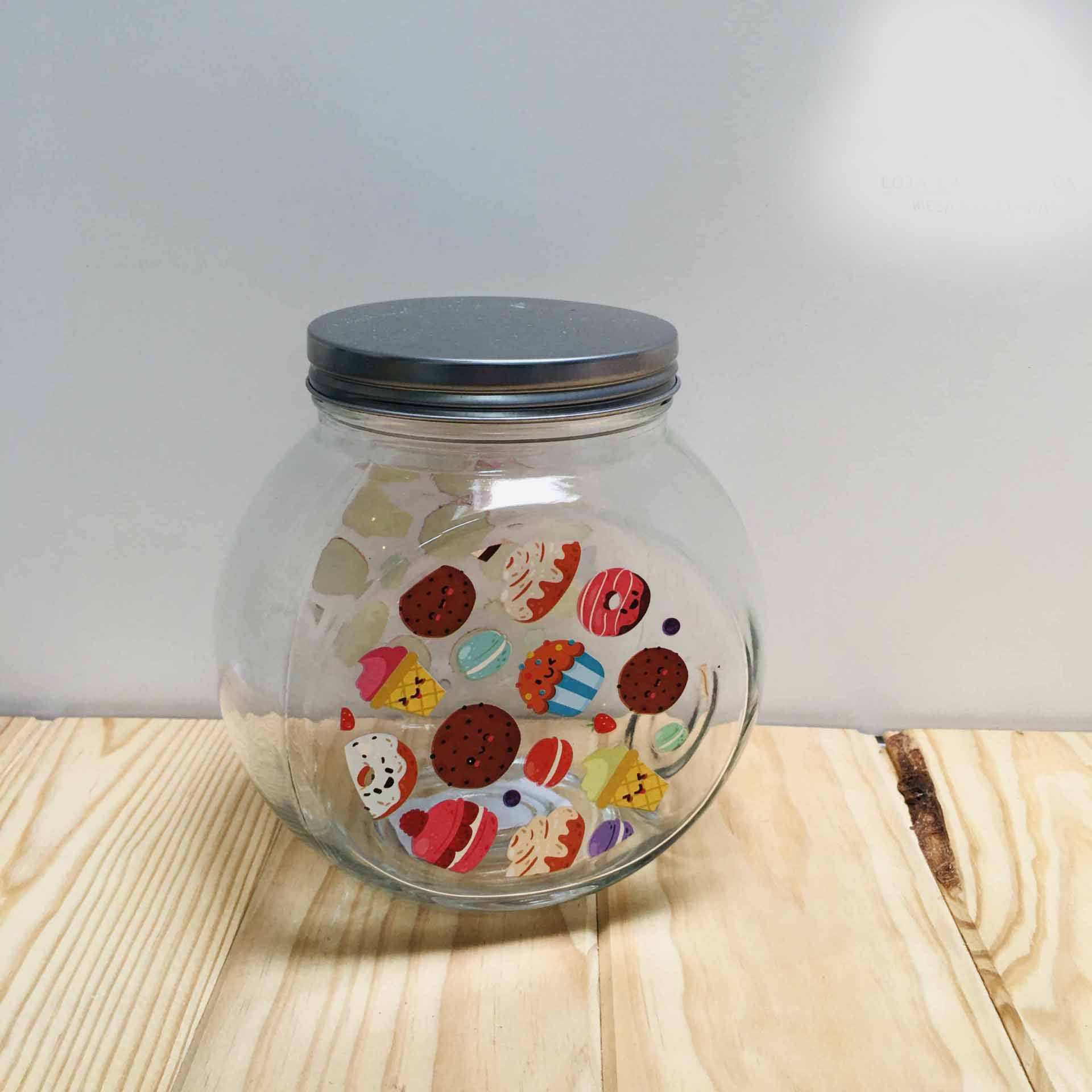Frasco de vidro redondo decorado com autocolantes coloridos de doces, em superfície de madeira