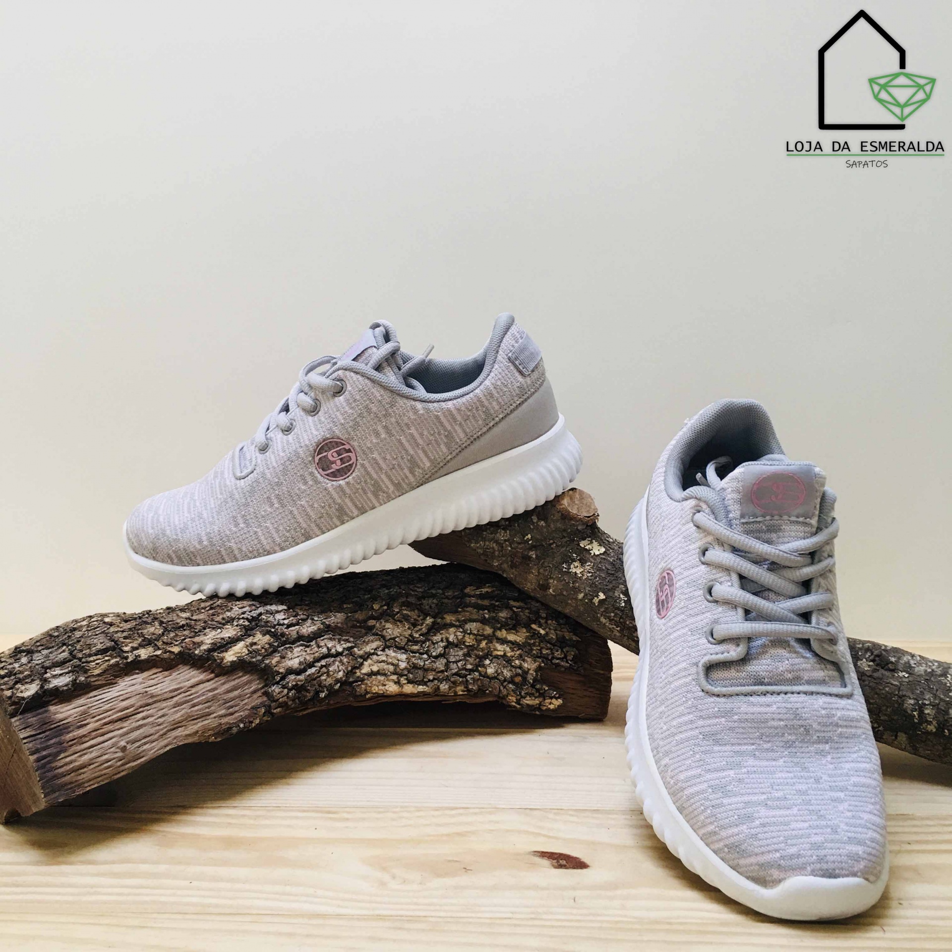Ténis cinzentos em tecido com sola branca e logo rosa em madeira clara