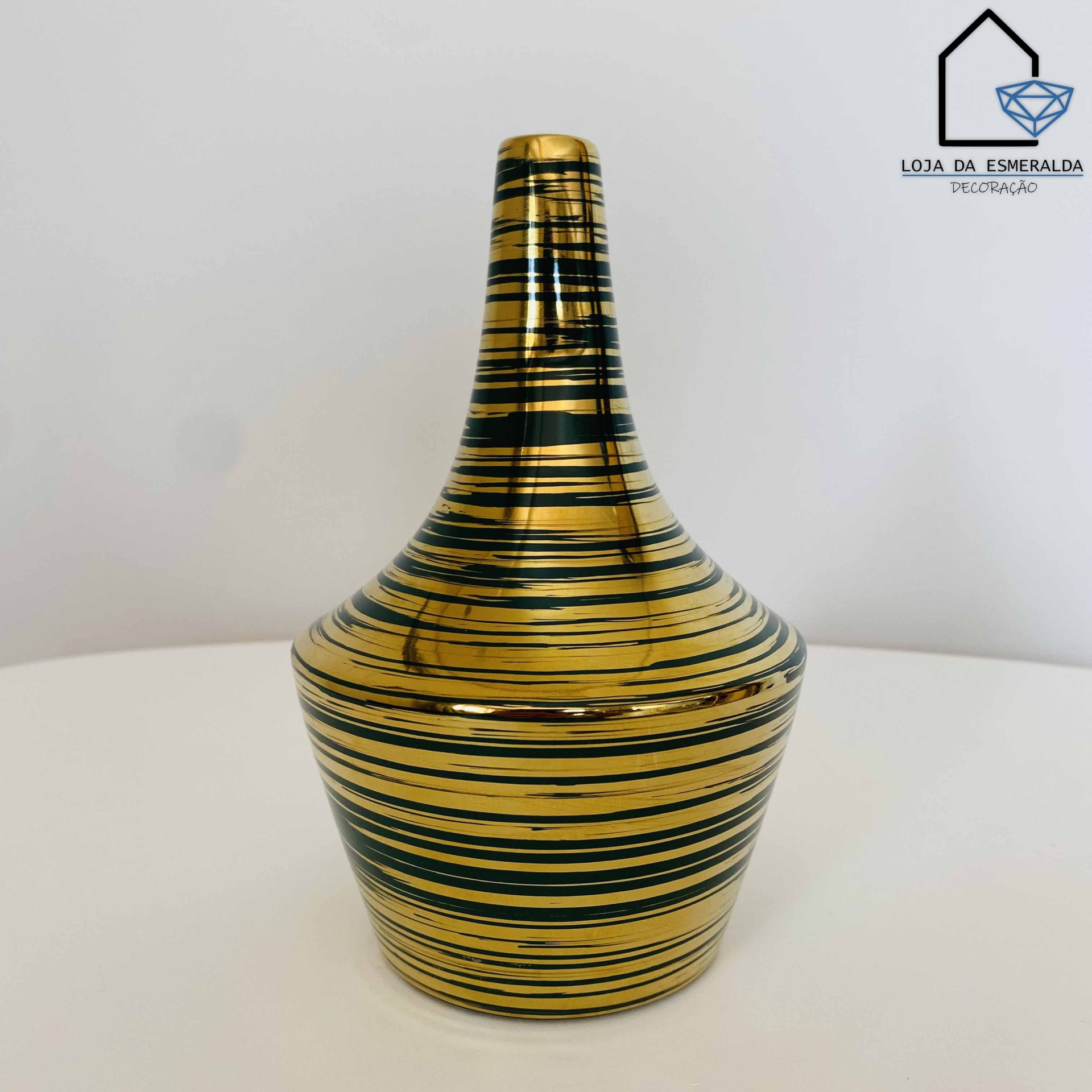 Recipiente decorativo dourado com linhas pretas horizontais sobre superfície branca