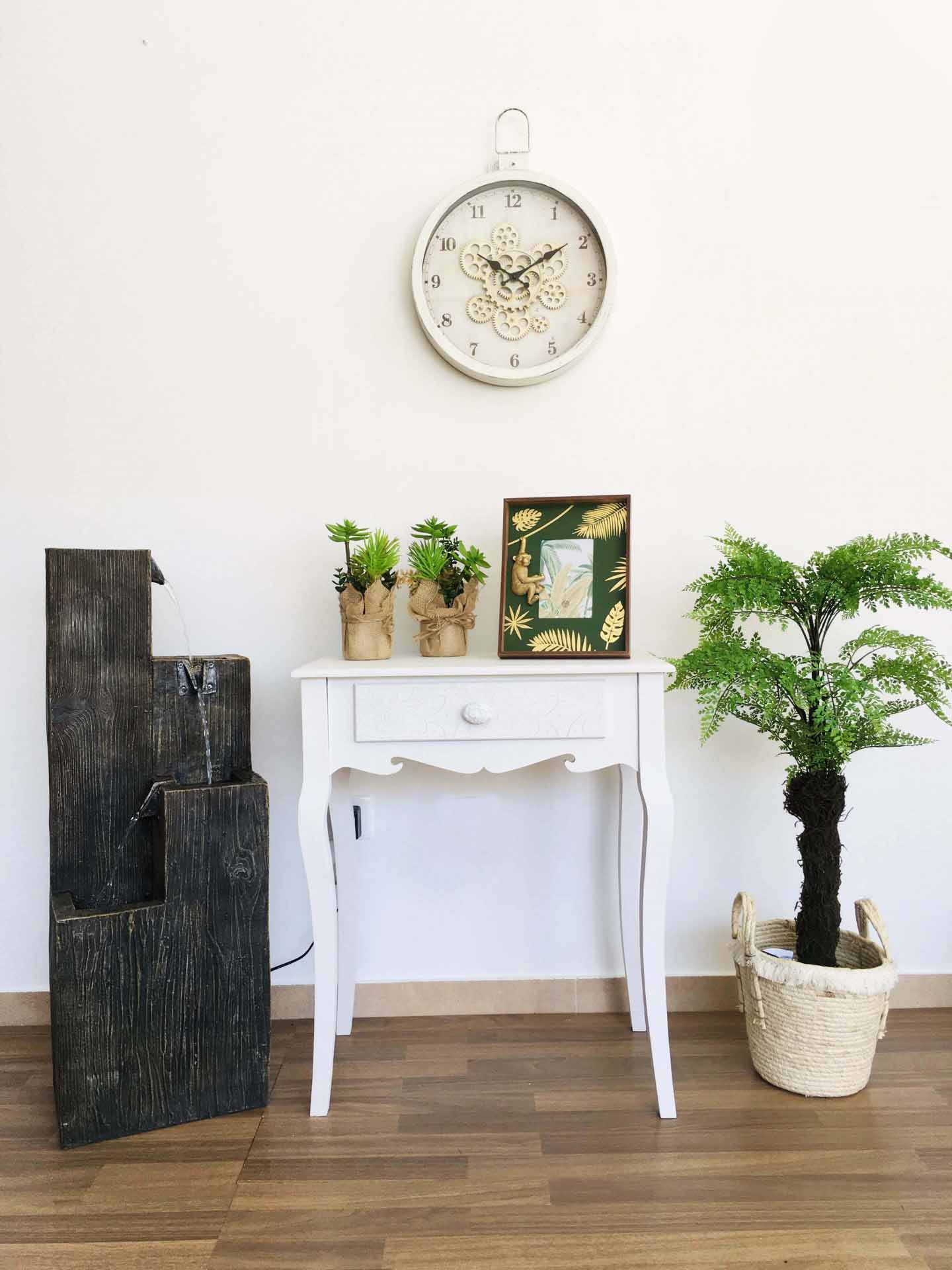 Relógio de parede, mesa branca, mini-vasos com suculentas e quadro decorativo em ambiente interior