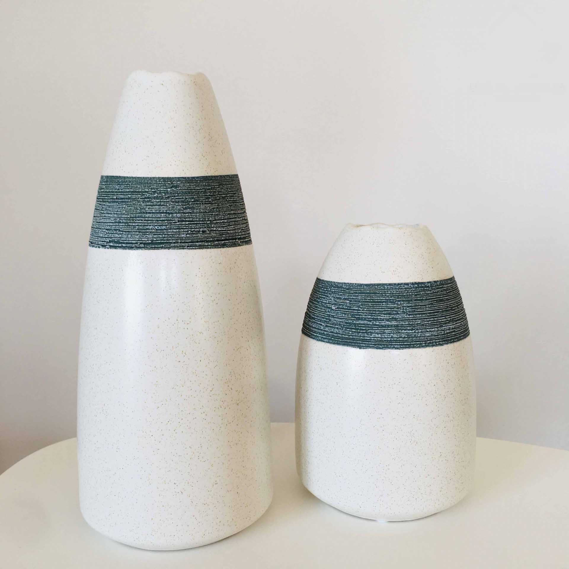 Dois vasos de cerâmica branca com faixa cinza texturizada numa superfície branca