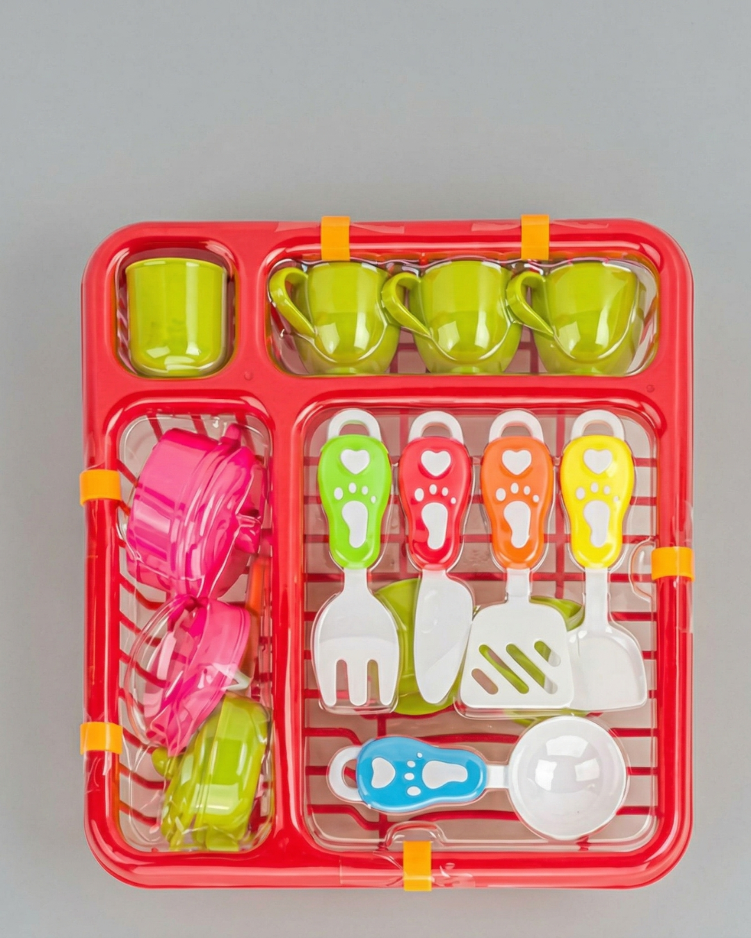 Conjunto de loiça de brincar com chávenas verdes, tachos rosa e verde, utensílios coloridos num tabuleiro vermelho.