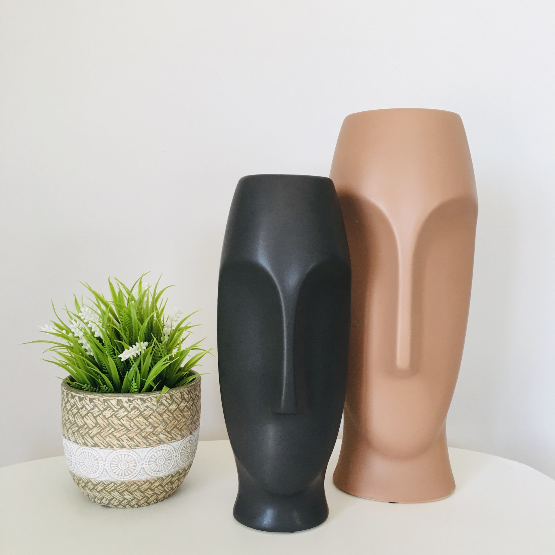 Dois vasos cerâmicos decorativos com formato de rosto e uma planta artificial num vaso menor ao lado
