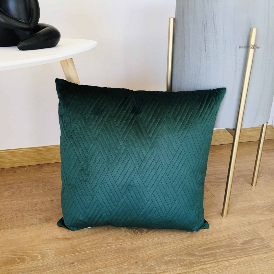 Almofada verde escura com padrão geométrico no chão ao lado de mesa e vaso.