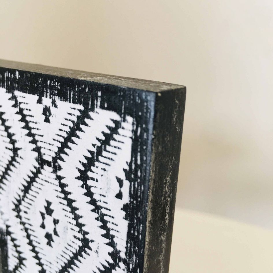 Quadro em madeira preta e branca com padrão geométrico em zig-zag.