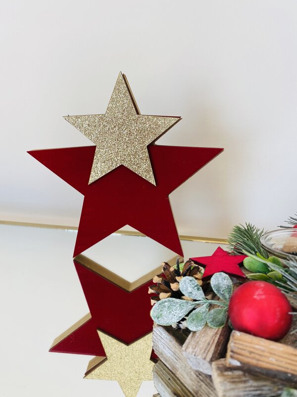 Estatueta decorativa estrela vermelha com estrela dourada glitter, em superfície espelhada junto a decoração natural