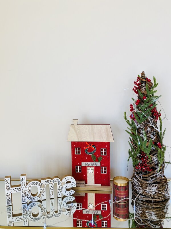 Decoração natalícia com casa vermelha, árvore pequena com bagas vermelhas, vela xadrez e placa branca Home Love