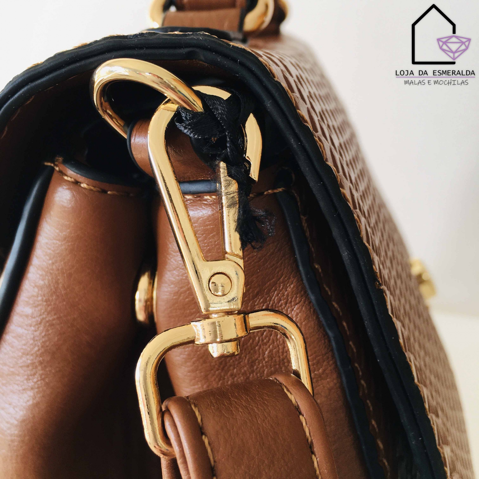 Detalhe de mala castanha com fecho dourado e textura trançada, fundo branco com logotipo da loja.
