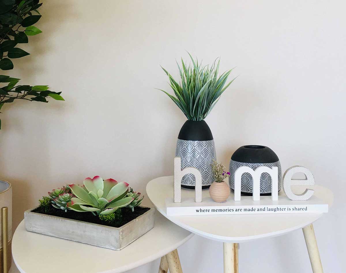 Plantas e decoração em duas mesas brancas com pernas de madeira clara