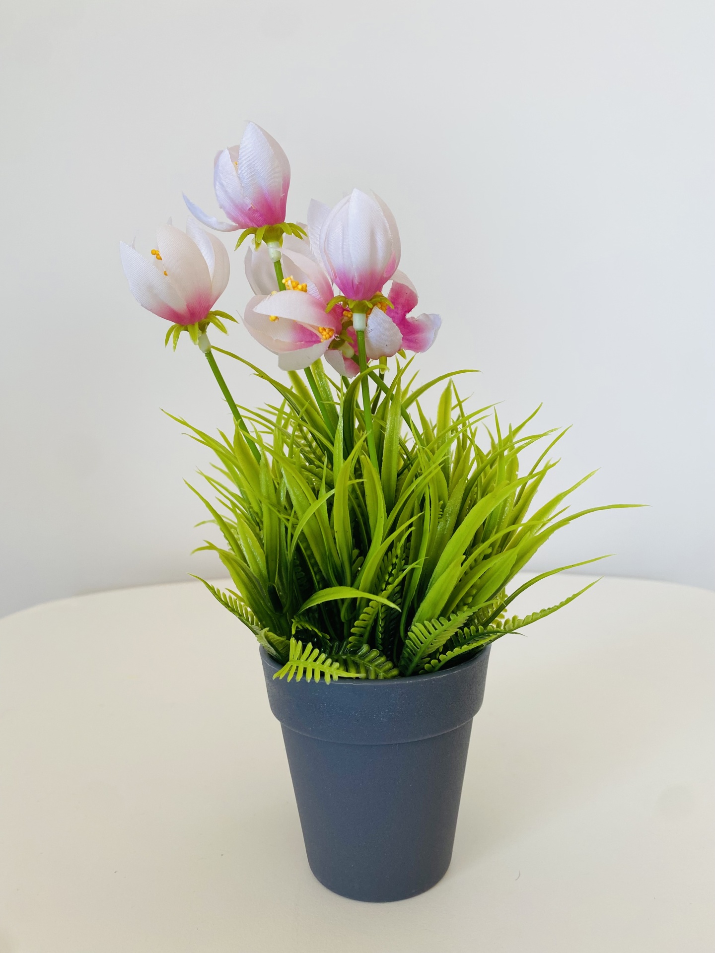 Vaso cinzento com planta artificial flores brancas e rosas sobre superfície branca