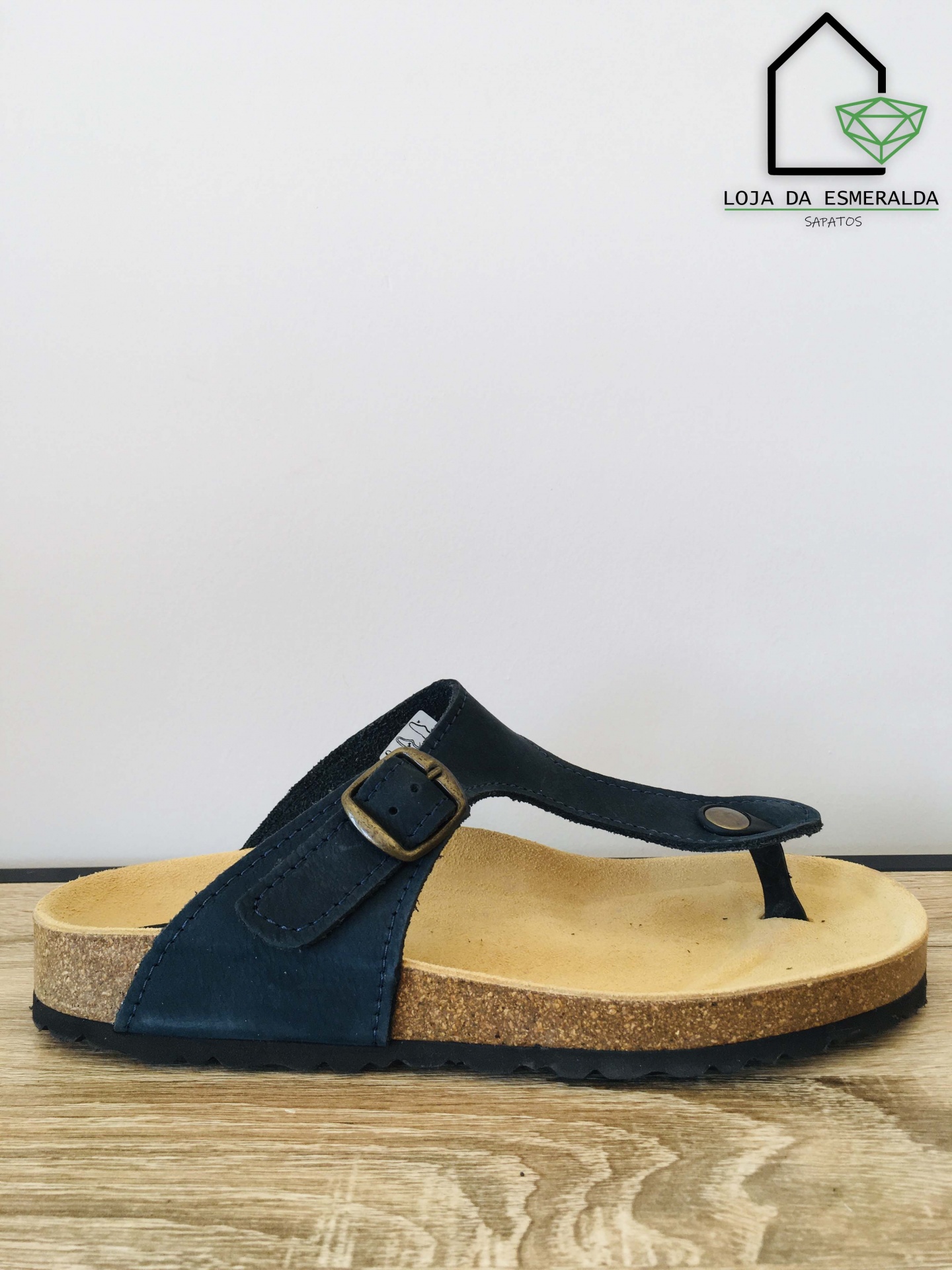 Sandália chinelo preta com sola de cortiça e logo da loja ao fundo