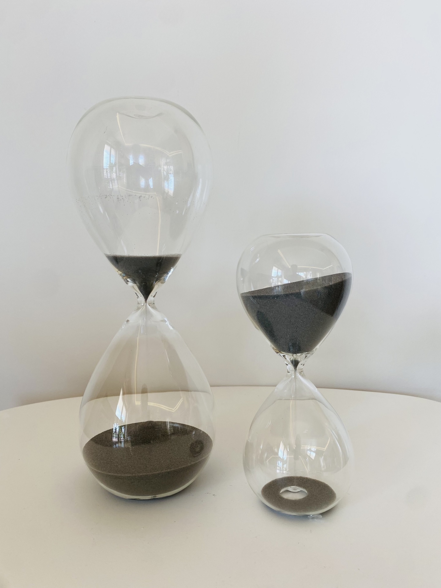 Dois relógios de areia transparentes com areia preta sobre superfície branca