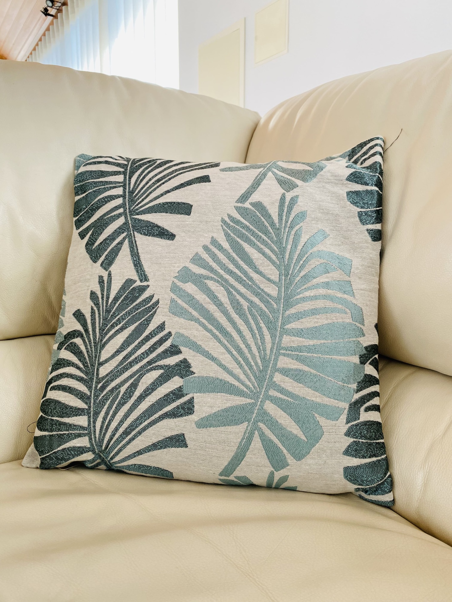 Almofada decorativa com padrão de folhas em sofá creme