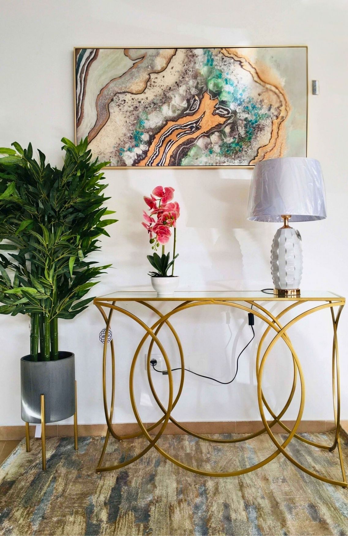 Aparador dourado e vidro com planta, flores artificiais e candeeiro num interior