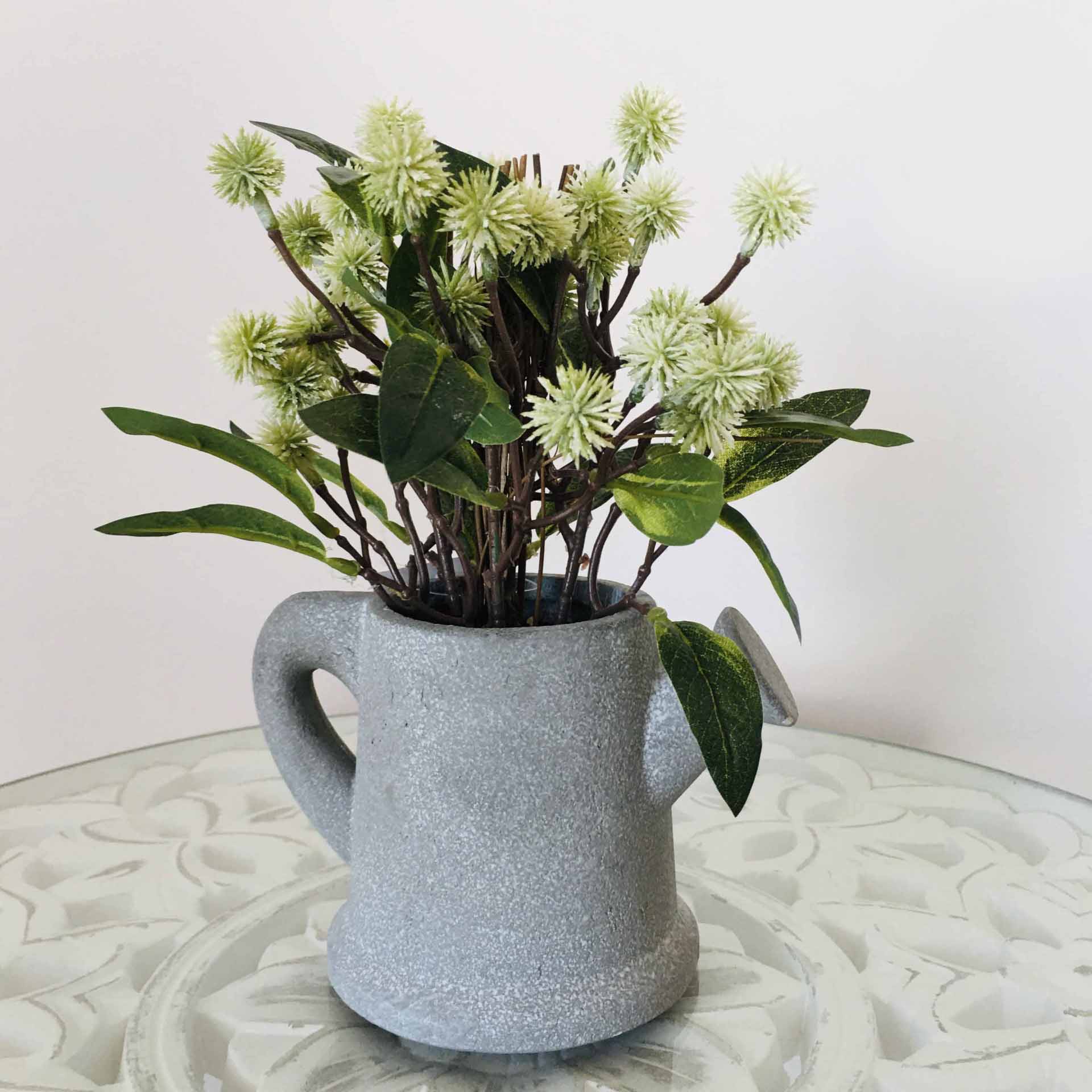 Vaso cinza claro com flores artificiais verdes e brancas em mesa branca