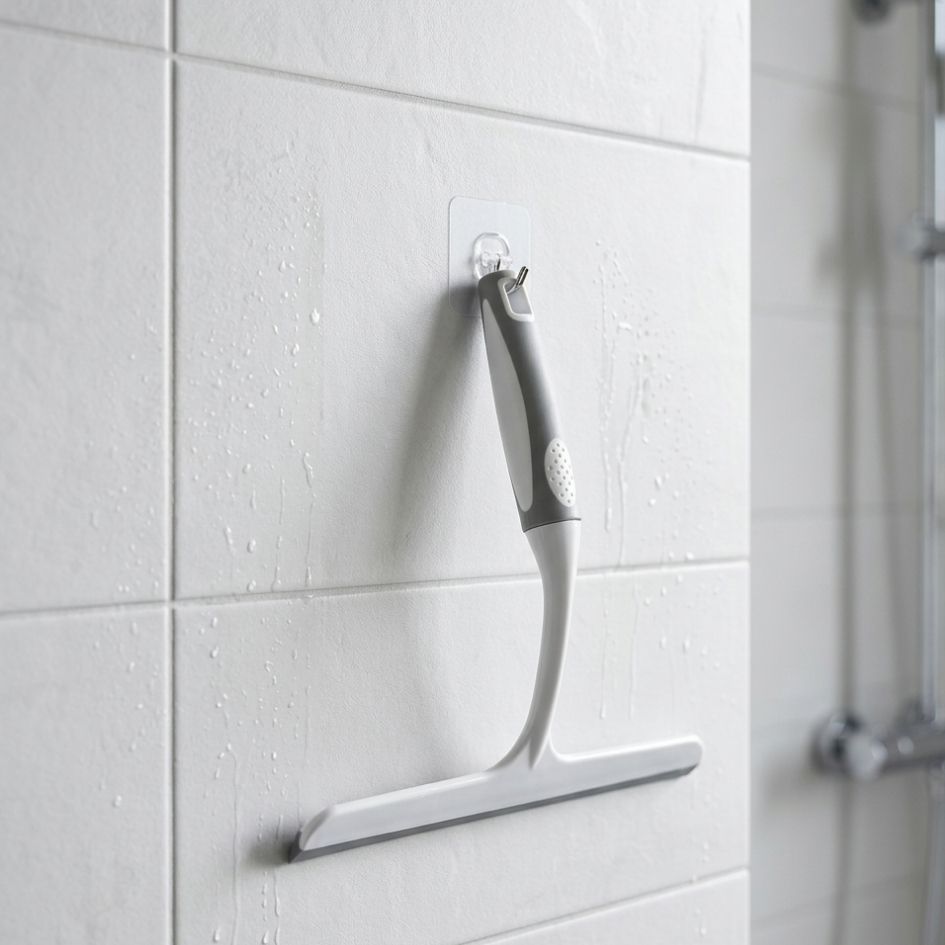 Raspador de banho cinzento e branco pendurado em azulejos brancos molhados