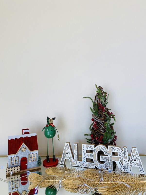 Decoração natalícia com casa em miniatura, figura de rena, árvore de Natal, letras ALEGRIA e ramos dourados.