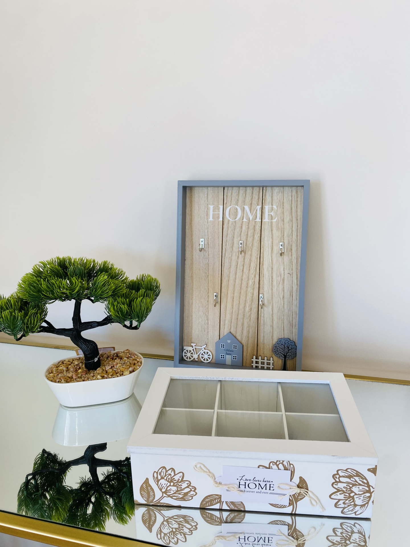 Organizador de madeira branco com vidro e decoração floral, quadro com texto HOME e planta artificial em vaso branco