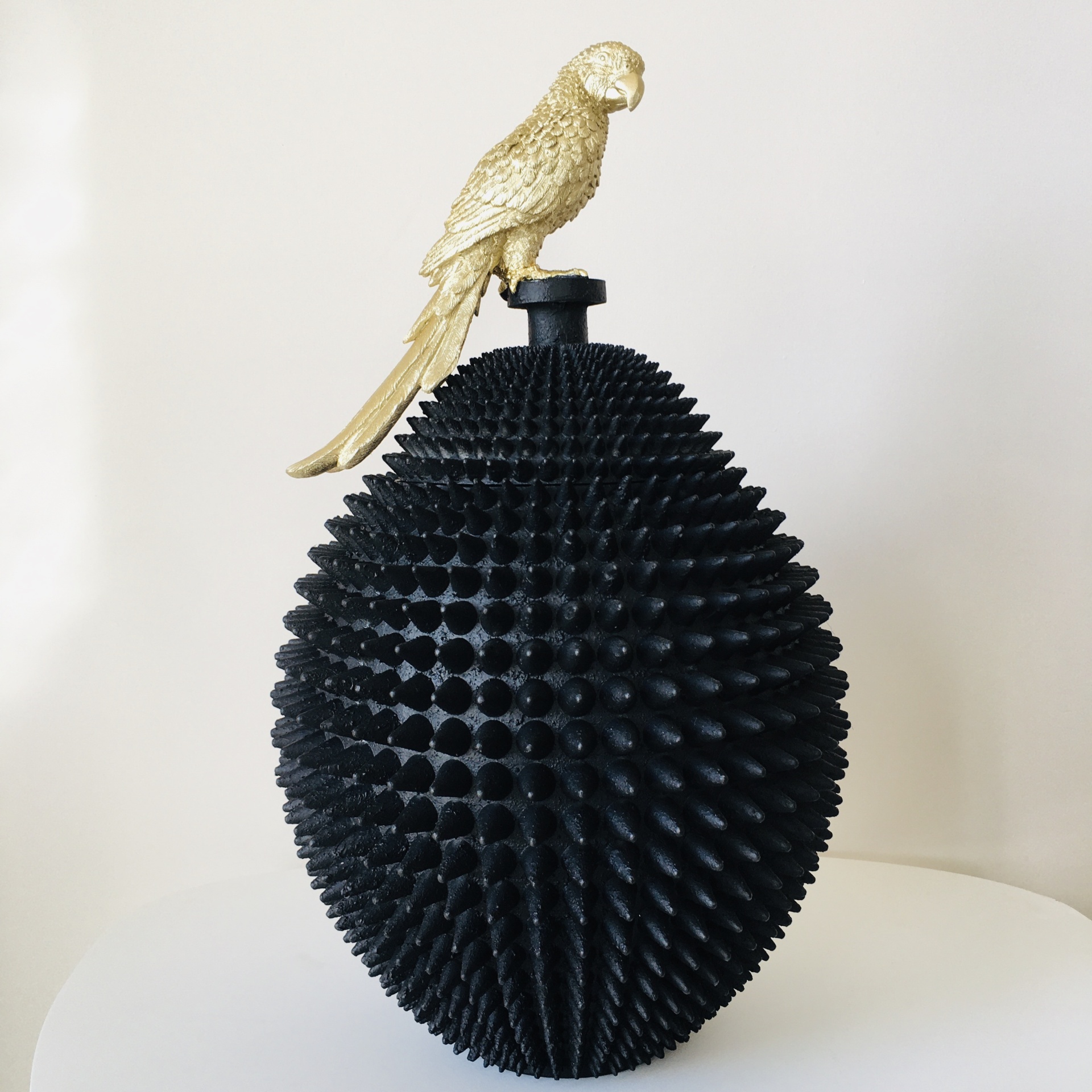 Garrafa preta com textura pontiaguda e pássaro dourado no topo