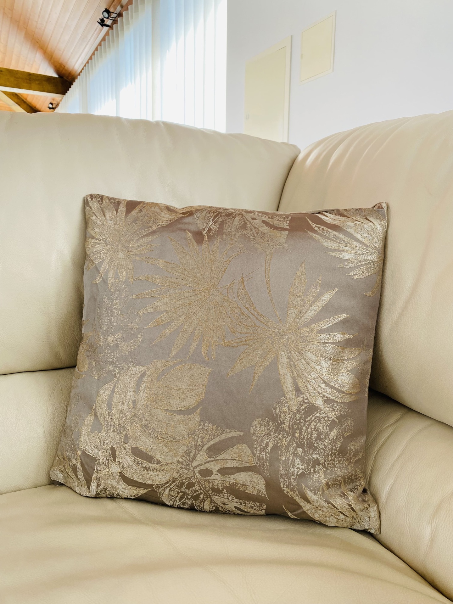 Almofada decorativa castanha com padrão de folhas douradas num sofá bege.