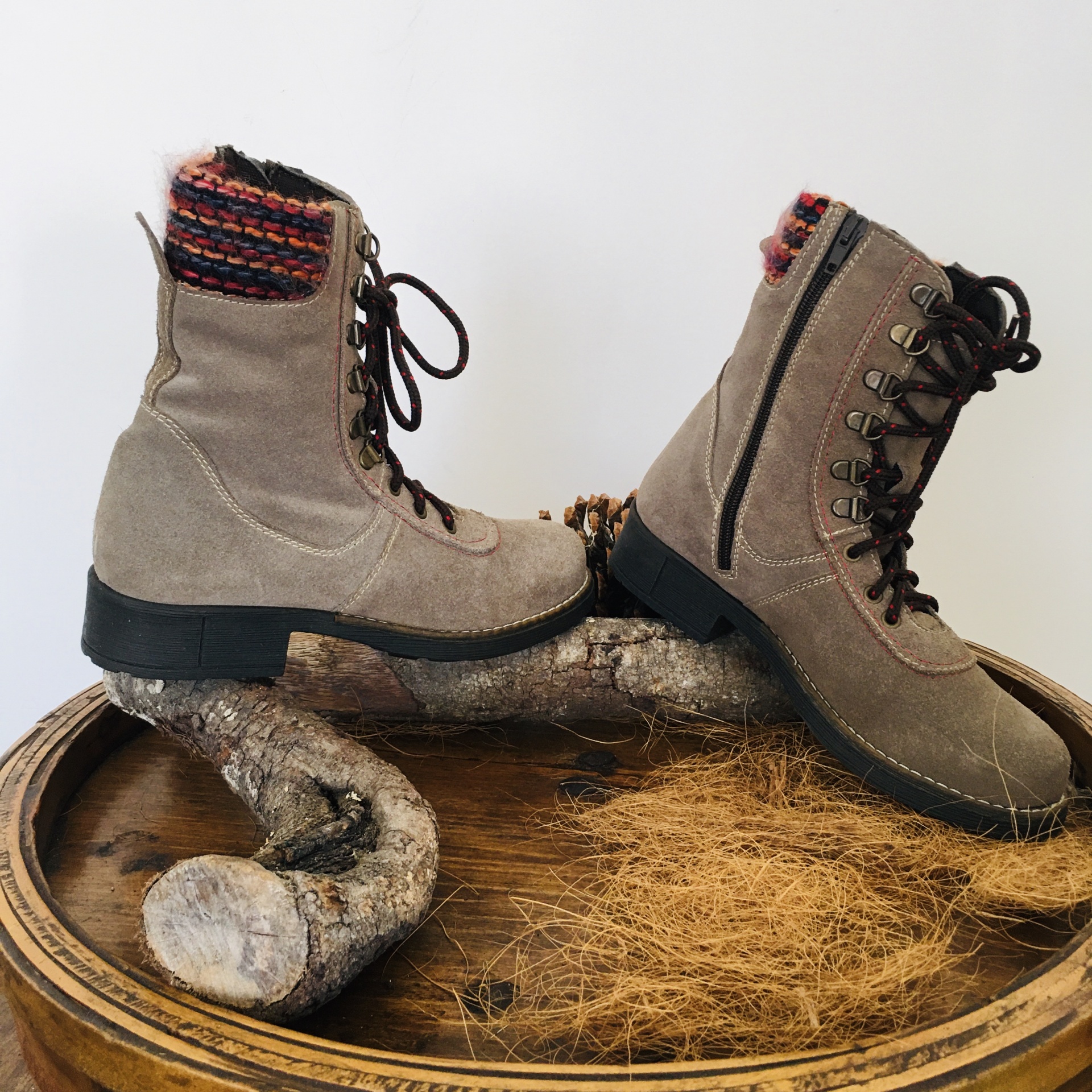 Botas de camurça bege com atacadores castanhos e forro colorido sobre tronco de madeira