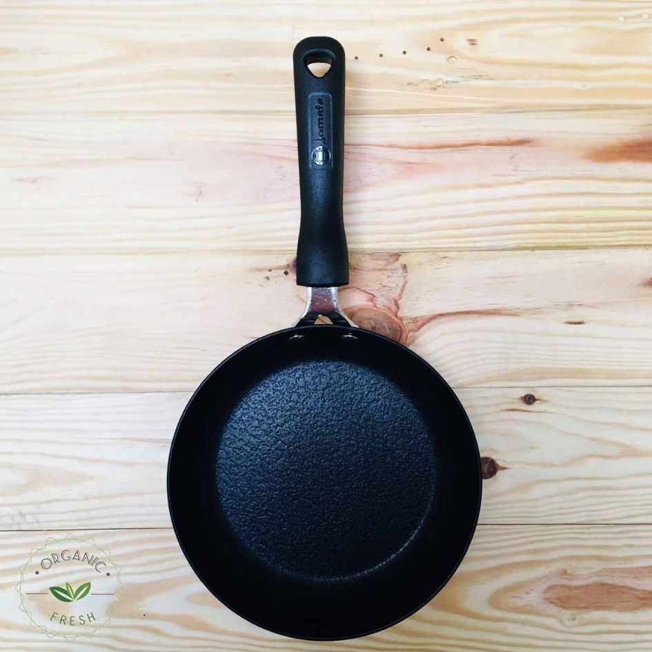 Frigideira preta antiaderente com pega preta sobre superfície de madeira clara