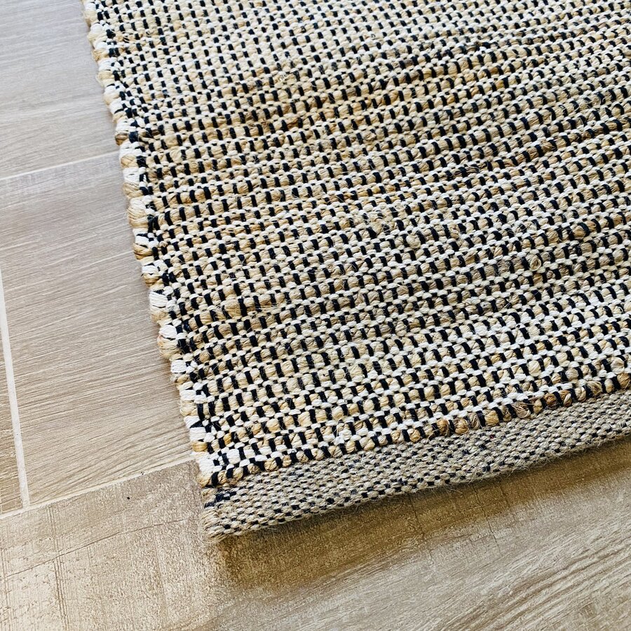 Tapete tecido quadriculado preto, branco e bege com franjas sobre piso de madeira clara