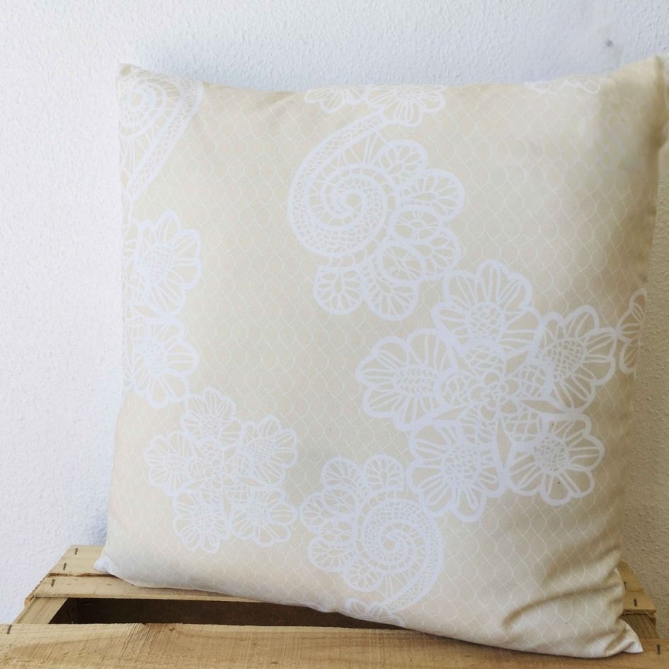 Almofada bege com padrão floral branco sobre superfície de madeira
