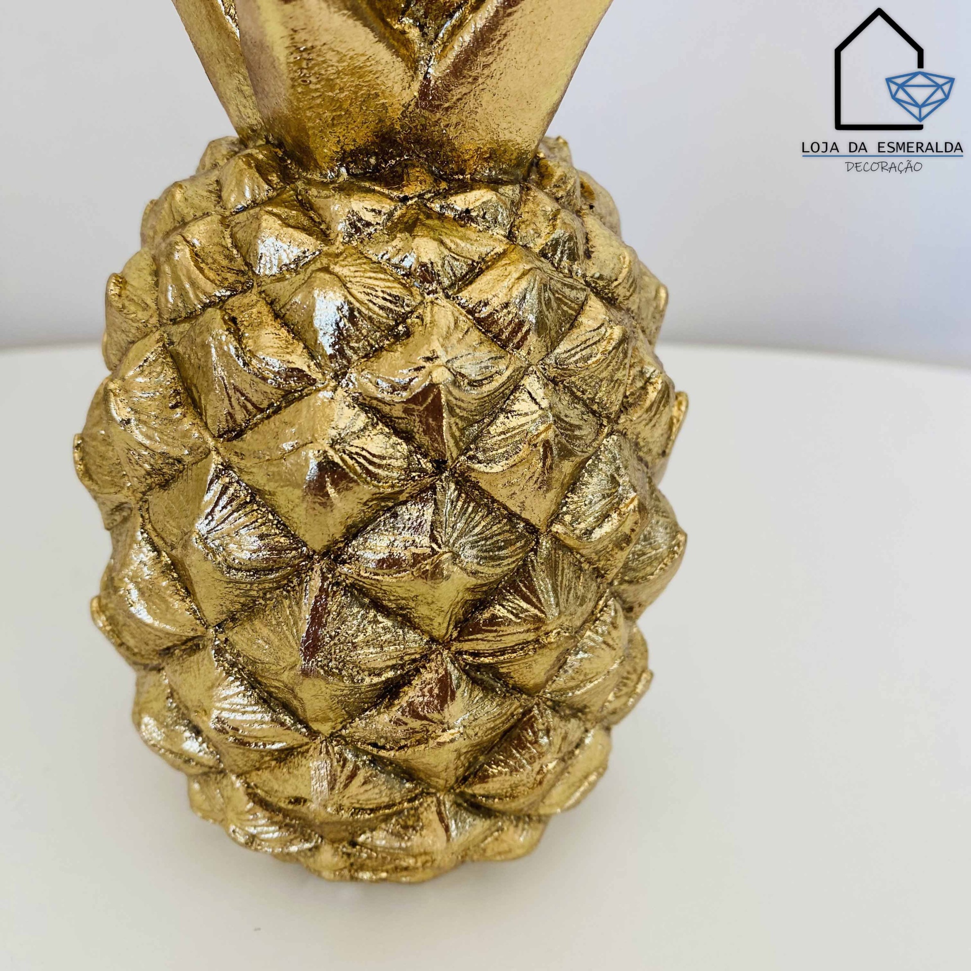 Estatueta dourada em forma de ananás com textura detalhada sobre superfície branca