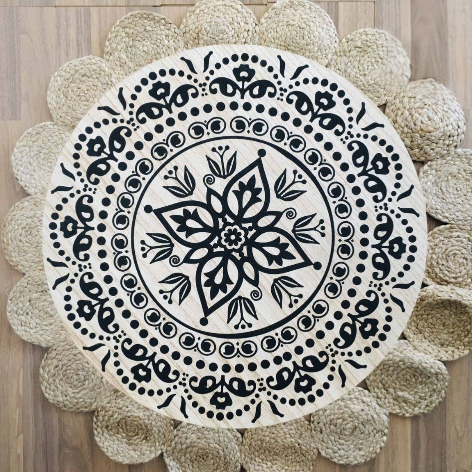 Mesa redonda de madeira com padrão floral preto sobre tapete trançado claro