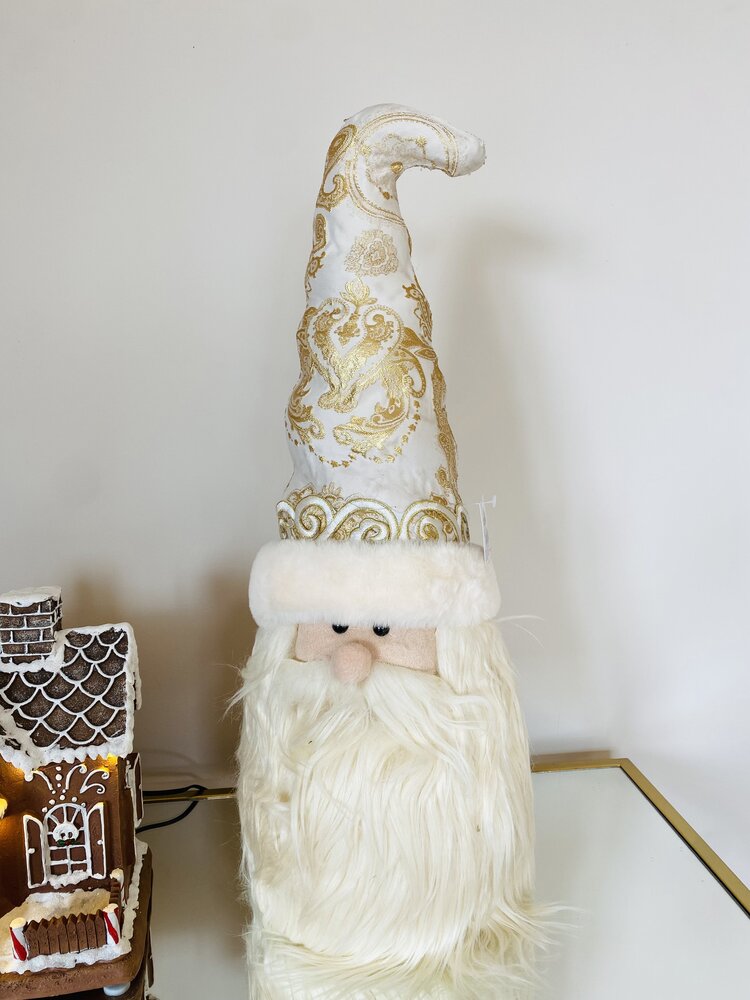 Figura decorativa de Pai Natal com chapéu alto branco e dourado e barba longa branca numa mesa branca
